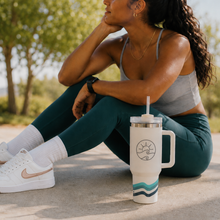 Load image into Gallery viewer, A woman in a gray sports bra and dark teal leggings sits outdoors on a concrete surface, with a white handled tumbler featuring a teal wave design and a sun-and-wave logo placed in front of her. She is wearing white sneakers with rose gold swooshes.
